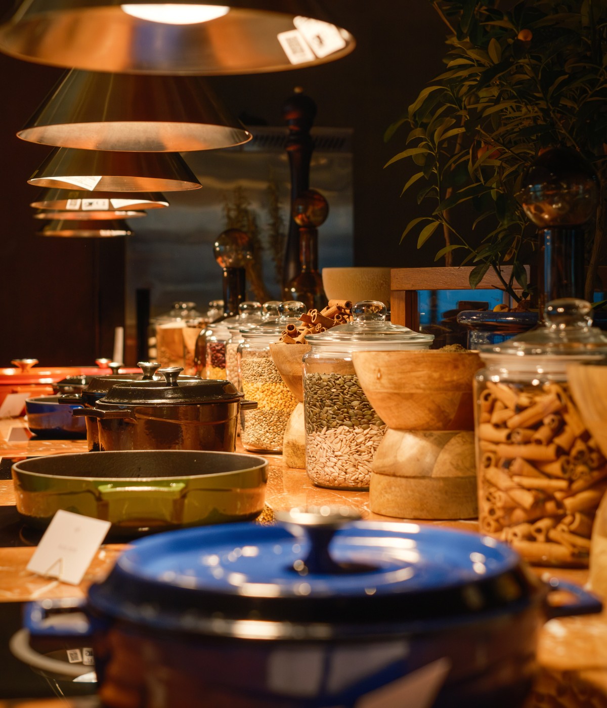 Warmly lit buffet with assorted jars of grains and spices, colorful pots, and bowls under lamps, creating a cozy and inviting atmosphere.