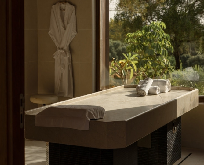 http://Sunlit%20spa%20room%20with%20a%20massage%20table,%20towels,%20and%20a%20hanging%20robe.%20A%20large%20window%20reveals%20lush%20greenery,%20creating%20a%20serene,%20tranquil%20atmosphere.