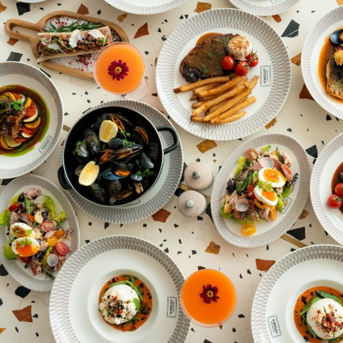 A vibrant spread of gourmet dishes, including seafood, steak, salads, and colorful drinks, arranged on a patterned table.