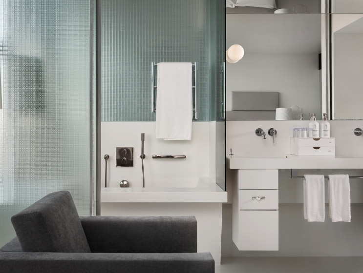 Modern bathroom with a minimalist design features a glass shower, white basin, and soft lighting. Neatly arranged toiletries and towels enhance serenity.