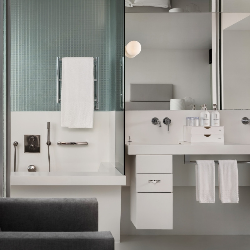 Modern bathroom with a minimalist design features a glass shower, white basin, and soft lighting. Neatly arranged toiletries and towels enhance serenity.