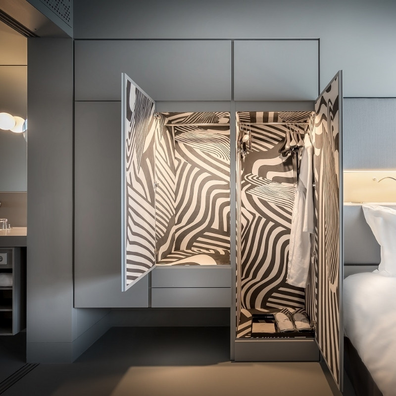 Open wardrobe with bold black and white zebra-striped interior, contrasting a minimalist gray bedroom. Modern, artistic, and striking design.