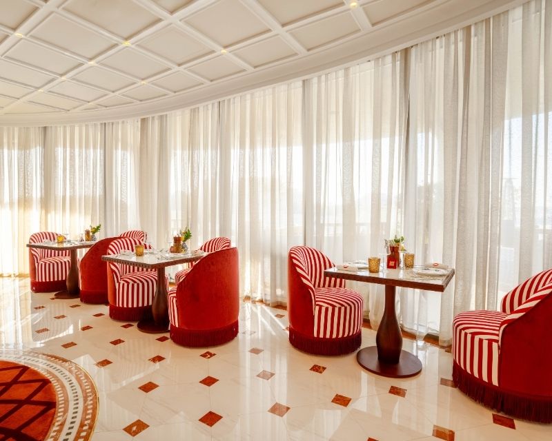 http://Cozy%20café%20with%20red%20and%20white%20striped%20chairs%20and%20round%20tables,%20set%20against%20large%20windows%20with%20sheer%20curtains.%20Warm%20natural%20light%20creates%20an%20inviting%20ambiance.