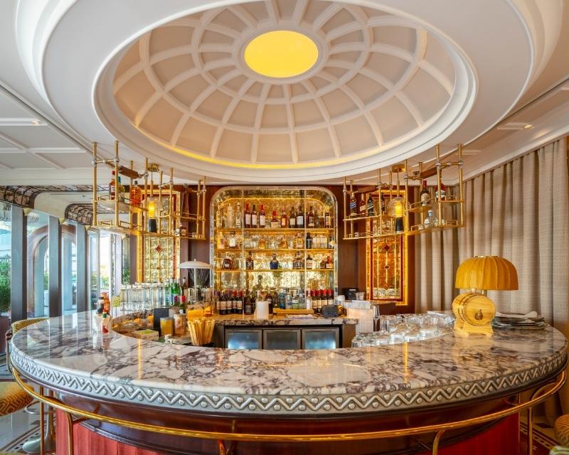 http://Elegant%20circular%20bar%20with%20a%20marble%20countertop,%20stocked%20shelves,%20and%20warm%20lighting.%20The%20ceiling%20has%20a%20domed%20design,%20creating%20a%20luxurious%20ambiance.