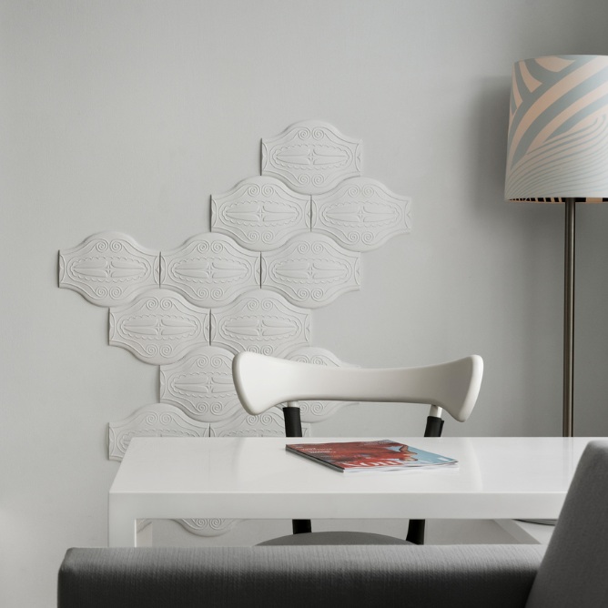 A modern interior featuring a white wall with decorative tiles, a sleek white table, and a minimalist chair beside a lamp.