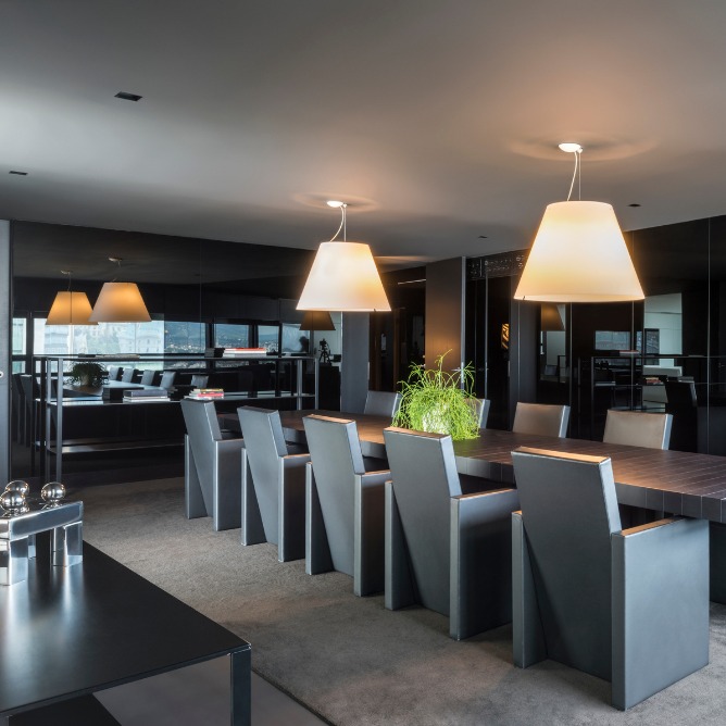 Sleek dining room with a long table, black high-back chairs, and two large pendant lights. A potted plant sits on the table, creating a modern, elegant feel.