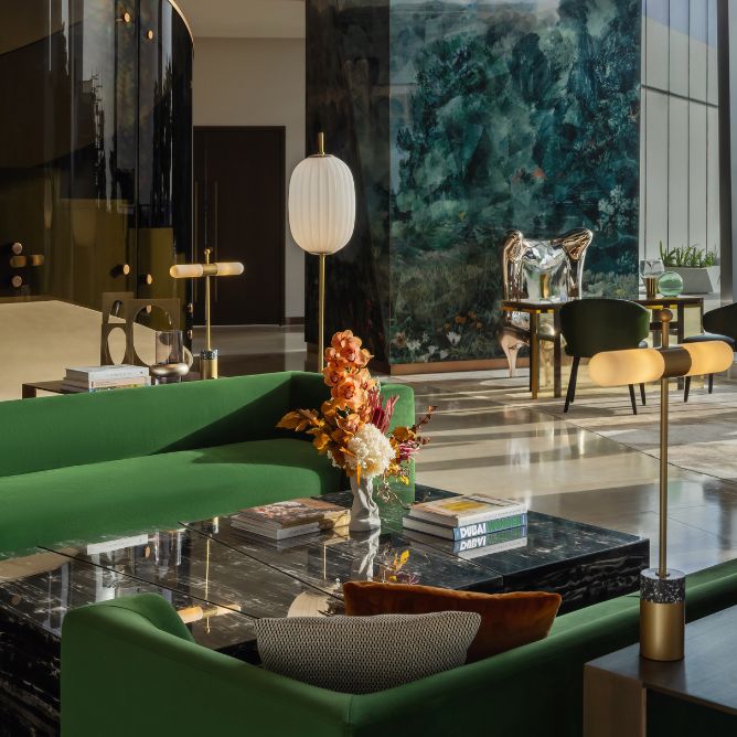 Stylish modern lounge featuring a green sofa, elegant decor, vibrant flowers, and large artwork against a sleek backdrop.