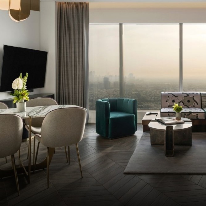 Modern living area featuring a glass window with a city view, stylish furniture, and a dining table. Warm lighting enhances the ambiance.