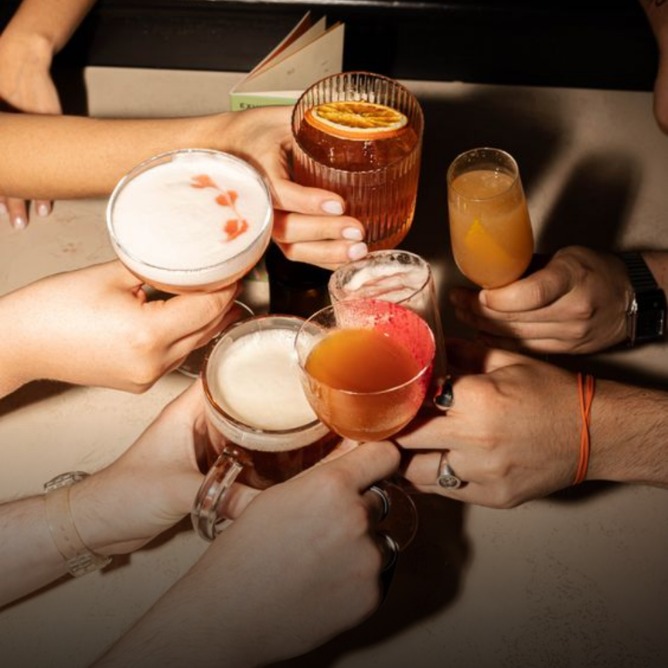 A group of hands holding various colorful cocktails, celebrating together at a lively gathering.