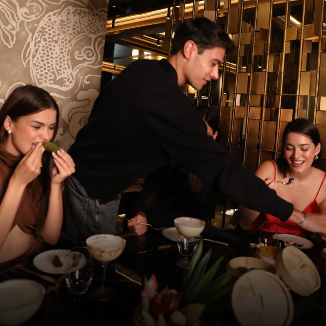 A server in a black sweater leans over a table, presenting food to a group of women enjoying a stylish dining experience.