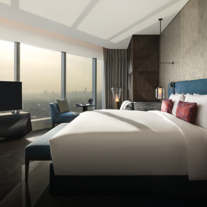 Luxurious hotel room with a large bed, plush pillows, and a panoramic city view through floor-to-ceiling windows. Modern decor with a serene, elegant ambiance.