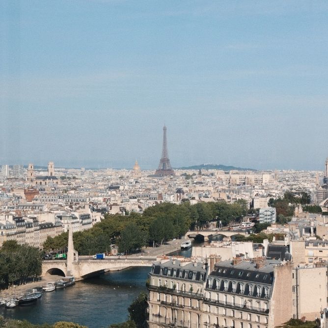Aerial view of Paris with the Seine River, bridges, buildings, and the Eiffel Tower in the background under a clear sky.