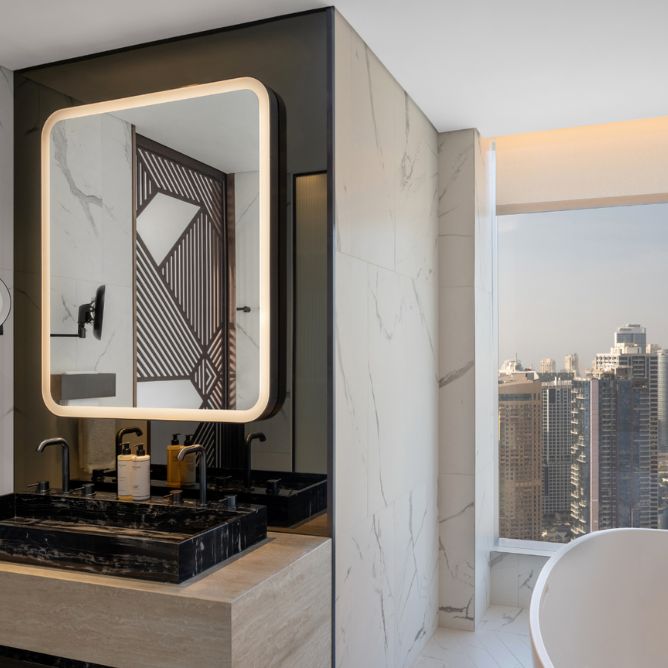 Luxurious bathroom with marble walls and a large mirror framed with soft lighting. Black sink fixtures, stylish geometric details, and a window with a city skyline view. Minimalist elegance.