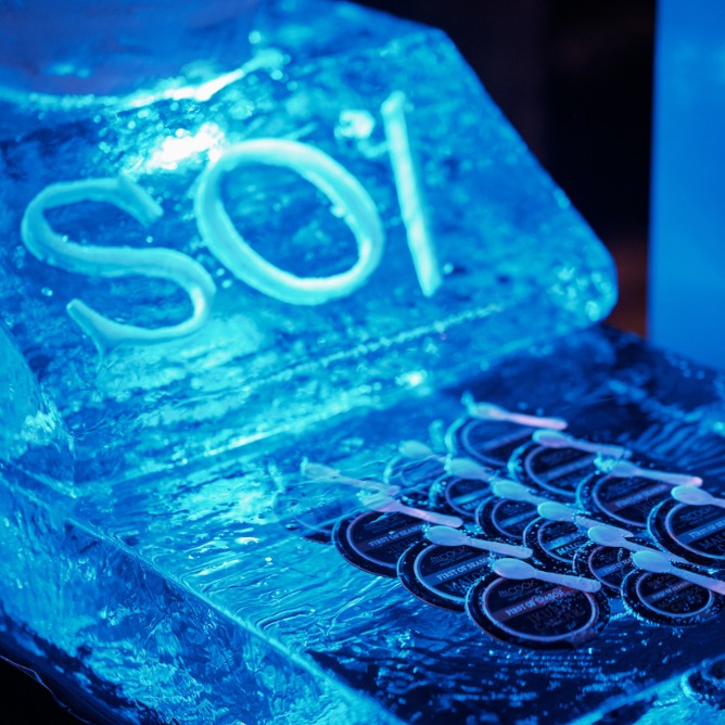 A luminous blue ice sculpture displays the word "Soi," with ornate patterns and circular designs underneath, creating a cool, artistic ambiance.
