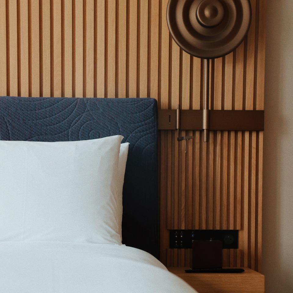 Modern bedroom with a blue upholstered headboard, white pillow, wooden slat wall, and unique circular wall lamp.