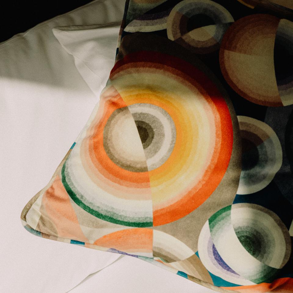 Decorative pillow with colorful concentric circle patterns resting on a white fabric surface.