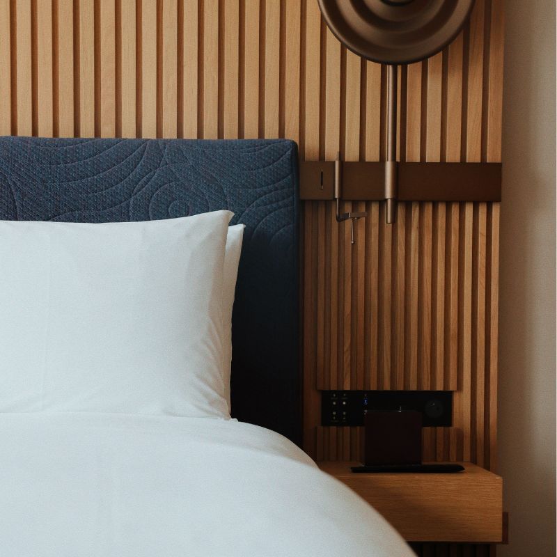 Modern bedroom with a blue upholstered headboard, white pillow, wooden slat wall, and unique circular wall lamp.