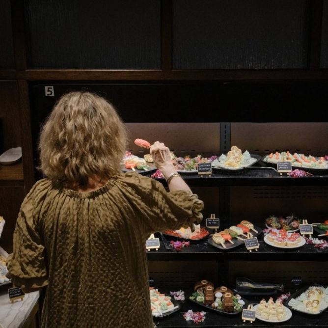 A woman seen from behind choosing a sweet treat from a multi-tiered dessert buffet display.