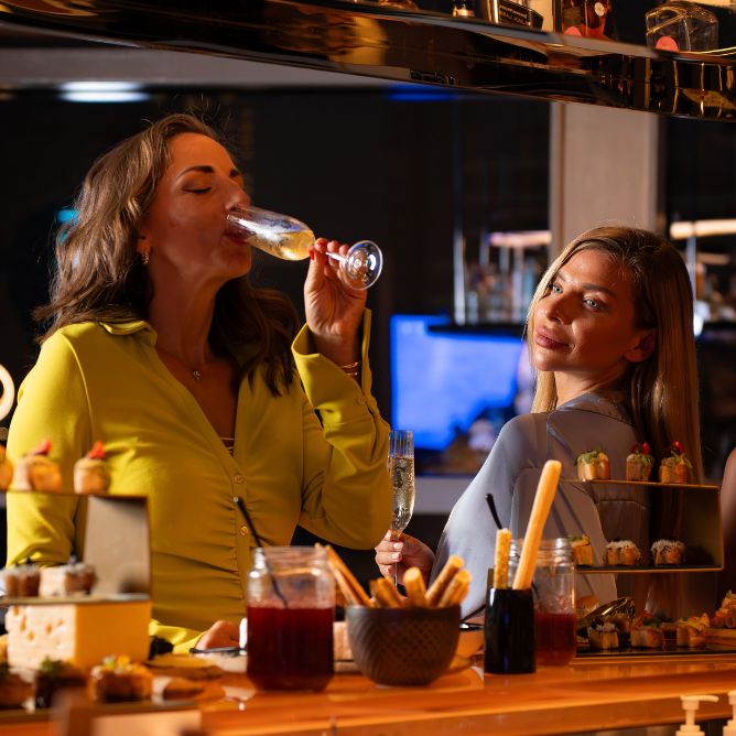 Women enjoying champagne and appetizers at a modern hotel bar counter.