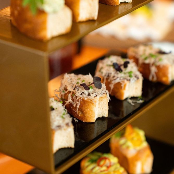 Close-up of a tiered appetizer stand featuring gourmet small bites and cheese toasts.