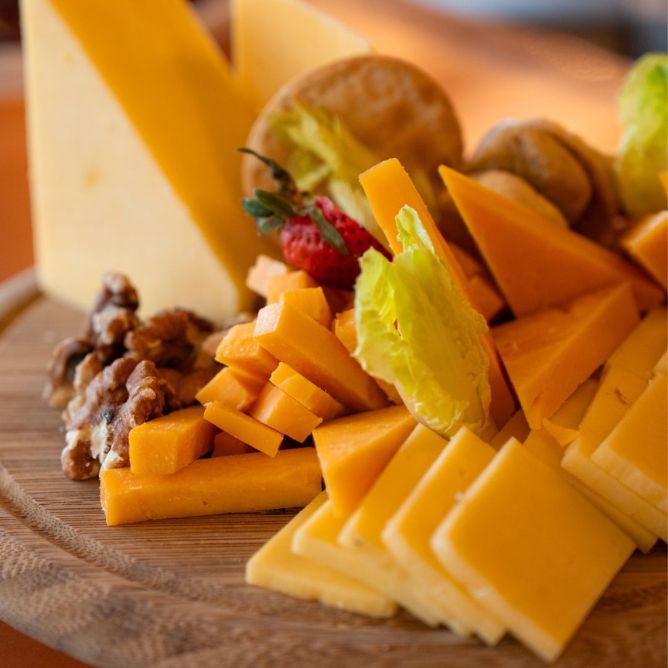 Rustic wooden cheese board with cheddar cheese, sliced varieties, walnuts, and fresh garnish.
