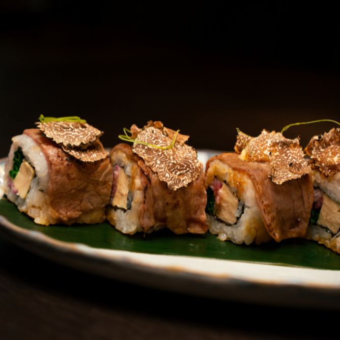 Gourmet seared wagyu beef sushi rolls topped with luxury black truffle shavings on a green leaf plate.