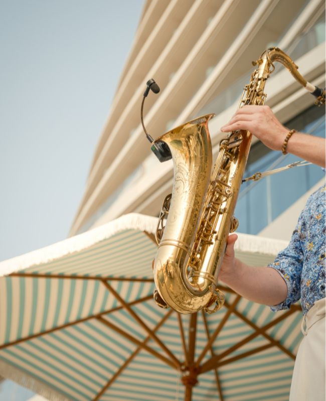 A man playing a saxophone on a sandy beach, with waves gently crashing in the background.