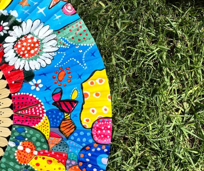 Close-up of a vibrant, hand-painted artistic fan resting on lush green grass.