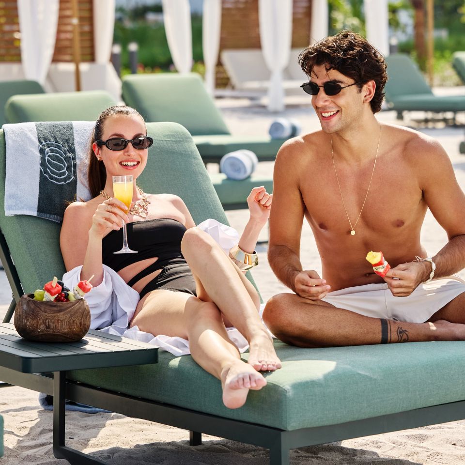 A man and woman relax on lounge chairs at the beach, enjoying the sun and ocean view.