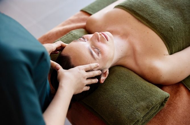 http://A%20woman%20lying%20down%20with%20eyes%20closed,%20enjoying%20a%20relaxing%20head%20and%20temple%20massage%20from%20a%20professional%20spa%20therapist,%20with%20soft%20green%20towels.