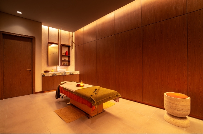 http://A%20private,%20minimalist%20massage%20room%20with%20warm%20wood-paneled%20walls,%20featuring%20a%20single%20heated%20treatment%20bed%20with%20an%20olive%20green%20blanket%20and%20a%20sculptural%20travertine%20stool.