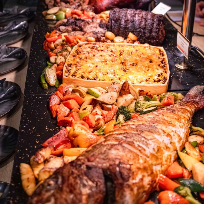 Gourmet Christmas buffet feast showing baked macaroni and cheese, roasted vegetables, whole baked fish, and carved meats on a serving platter.