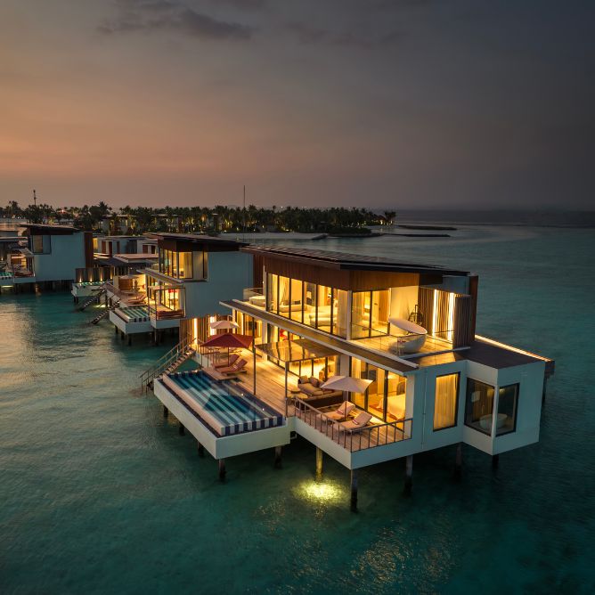Scenic view of overwater villas at sunset, with colorful skies and tranquil waters creating a serene atmosphere.